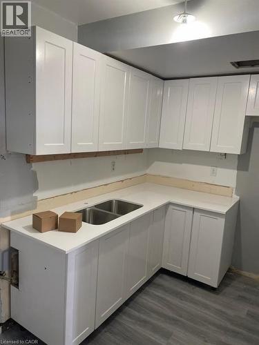 Corner kitchen area featuring white shaker-style cabinetry, a double-basin stainless steel sink, light-toned countertops, and wood-finish flooring - 150 Charlton Avenue E Unit# 708, Hamilton, ON 