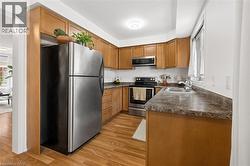Kitchen featuring wood-finish flooring, wood cabinetry, stainless steel appliances, a double basin sink, and a window - 