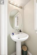 Pedestal sink with a polished chrome faucet, an oval mirror, and a three-bulb vanity light fixture - 