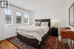 Bedroom featuring wood-finish flooring, white walls, and three grid-pattern windows - 