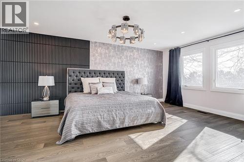 Wood-finish flooring throughout, featuring a tufted headboard, recessed ceiling lighting, a contemporary chandelier, and a decorative accent wall - 1320 Monmouth Drive, Burlington, ON 