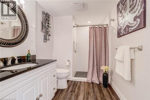 Bathroom featuring a white vanity with a dark countertop, an oval mirror, a walk-in shower, and wood-finish flooring - 1320 Monmouth Drive, Burlington, ON 