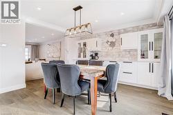 Dining area featuring wood-finish flooring, a linear chandelier, crown molding, and a built-in buffet with white cabinetry and a stone-finish backsplash - 