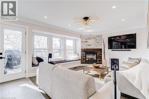Living area featuring a corner fireplace with a wood-finish accent wall, multiple windows, built-in window seating, and wood-look flooring - 1320 Monmouth Drive, Burlington, ON 