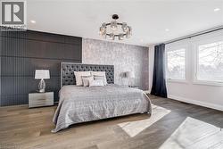 Wood-finish flooring throughout, featuring a tufted headboard, recessed ceiling lighting, a contemporary chandelier, and a decorative accent wall - 