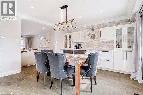Dining area featuring wood-finish flooring, a linear chandelier, crown molding, and a built-in buffet with white cabinetry and a stone-finish backsplash - 1320 Monmouth Drive, Burlington, ON 