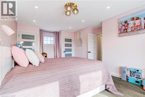 Bedroom featuring recessed lighting, a modern ceiling fixture, wood-finish flooring, and white interior doors with opaque glass panels - 1320 Monmouth Drive, Burlington, ON 