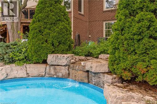 Swimming pool with a blue tiled border, surrounded by natural stone landscaping and mature evergreen shrubs - 1320 Monmouth Drive, Burlington, ON 