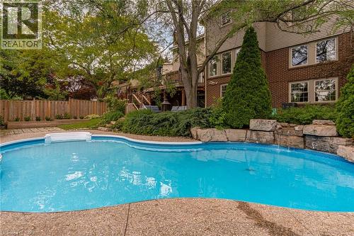 Free-form swimming pool with integrated waterfall feature, surrounded by exposed aggregate concrete decking - 1320 Monmouth Drive, Burlington, ON 