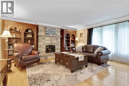 Living room featuring a stone fireplace with hearth, wood-finish flooring, and crown molding - 110 Grand Ridge Drive, Cambridge, ON 