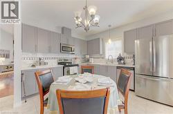Kitchen featuring light gray cabinetry, stainless steel appliances, white subway tile backsplash with decorative accent, and a single basin sink - 