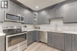 Contemporary kitchen featuring gray shaker-style cabinetry, white countertops, and stainless steel appliances - 