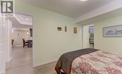 Bedroom featuring light green walls, wood-finish flooring, a recessed lighting fixture, and a doorway opening to a secondary space with a partial view of a kitchen island - 
