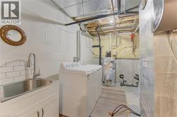 Utility space featuring a stainless steel sink with a high-arc faucet, white subway tile backsplash, and white cabinetry - 