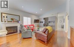 Living area featuring wood-finish flooring, a white mantel fireplace, and a built-in media center with display cabinetry - 