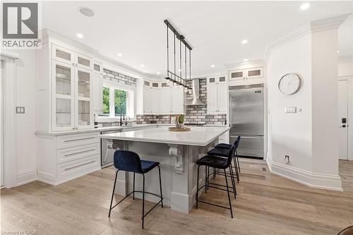 Gourmet kitchen featuring a large central island, light wood-finish flooring, white shaker-style cabinetry with glass accents, stainless steel appliances, and a subway tile backsplash - 336 Newbold Court, Burlington, ON 