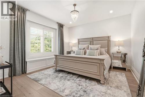 Bedroom featuring light wood-finish flooring, white walls, and a large window with white plantation shutters - 336 Newbold Court, Burlington, ON 