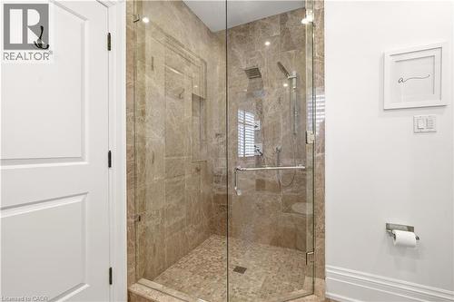 Glass-enclosed shower featuring full-height stone tile walls, a rain showerhead, a handheld shower fixture, and a pebble-style floor - 336 Newbold Court, Burlington, ON 