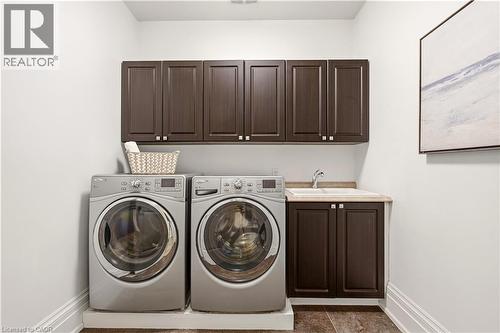 Dedicated laundry area featuring dark wood-finish cabinetry with silver hardware, a built-in sink with a countertop, and durable flooring - 336 Newbold Court, Burlington, ON 