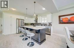 Modern kitchen featuring a dark island with a light countertop, stainless steel appliances, white cabinetry, and wood-finish flooring - 