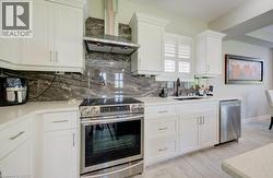Kitchen featuring white cabinetry, light-toned countertops, a stainless steel range with a coordinating hood, a dark patterned backsplash, and light wood-finish flooring - 