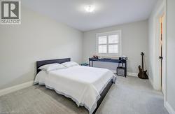 Spacious bedroom featuring light neutral wall tones, plush gray carpeting, and a window with white louvered shutters - 