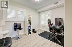 Flexible room featuring two windows with white plantation shutters, light gray wall paint, and wood-finish flooring - 