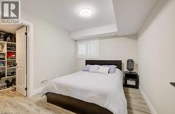 Bedroom featuring wood-finish flooring, a window with white louvered shutters, a built-in closet with shelving, and a flush-mount ceiling light fixture - 