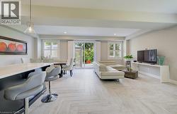 Open-concept living space featuring wood-finish flooring, recessed lighting, white plantation shutters, and a sliding glass door leading to outdoor greenery - 