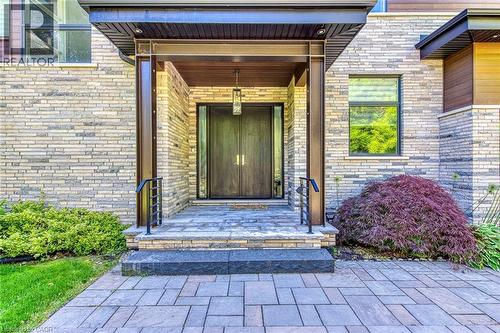 Modern entry featuring stacked stone facade, double wood-panel doors, and a stone-tiled porch - 2104 Devon Road, Oakville, ON 