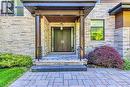 Modern entry featuring stacked stone facade, double wood-panel doors, and a stone-tiled porch - 2104 Devon Road, Oakville, ON 