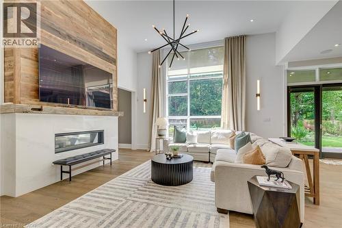 Spacious living area featuring a wood-finish accent wall, linear fireplace with white surround, high ceilings, large floor-to-ceiling windows, and wood-finish flooring - 2104 Devon Road, Oakville, ON - Indoor Photo Showing Living Room With Fireplace