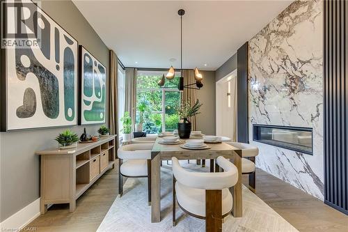 Dining area featuring wood-finish flooring, a linear fireplace with a stone surround, and an integrated wood-finish console with open shelving - 2104 Devon Road, Oakville, ON - Indoor Photo Showing Dining Room With Fireplace