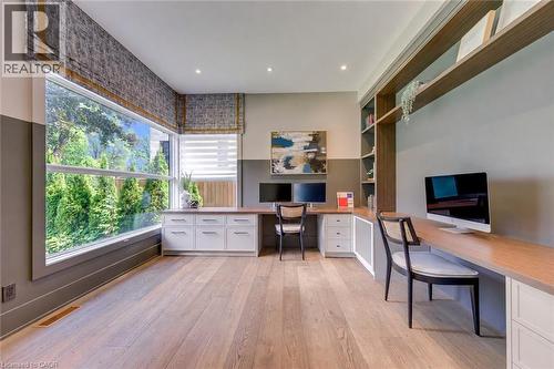 Spacious room featuring wood-finish flooring, a large picture window, built-in desks with white cabinetry, and integrated shelving - 2104 Devon Road, Oakville, ON - Indoor Photo Showing Office