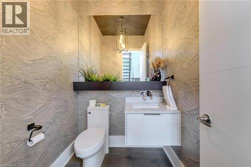 Powder room featuring textured wall covering, a wall-mounted vanity with an integrated sink, dark wood-finish flooring, and a contemporary pendant light fixture - 2104 Devon Road, Oakville, ON - Indoor Photo Showing Bathroom