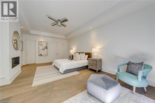 Expansive room featuring wood-finish flooring, a contemporary fireplace, tray ceiling with recessed lighting and a ceiling fan, and white paneled doors - 2104 Devon Road, Oakville, ON - Indoor Photo Showing Bedroom