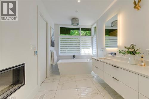 Modern bathroom featuring a freestanding soaking tub, a dual-sink vanity with a quartz-finish countertop, an illuminated mirror, and large format marble-finish floor tiles - 2104 Devon Road, Oakville, ON - Indoor