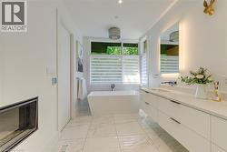 Modern bathroom featuring a freestanding soaking tub, a dual-sink vanity with a quartz-finish countertop, an illuminated mirror, and large format marble-finish floor tiles - 