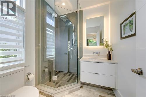 Modern bathroom featuring a glass-enclosed shower with multiple showerheads, a floating vanity with an integrated sink, an illuminated mirror, and wood-finish flooring - 2104 Devon Road, Oakville, ON - Indoor Photo Showing Bathroom