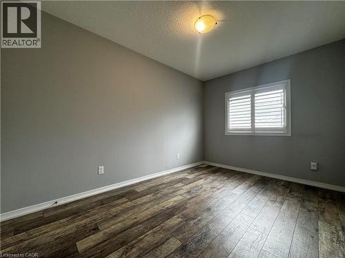 Room with wood-finish flooring, neutral gray walls, and white plantation shutters on the window - 13 Sorrento Street, Kitchener, ON - Indoor Photo Showing Other Room