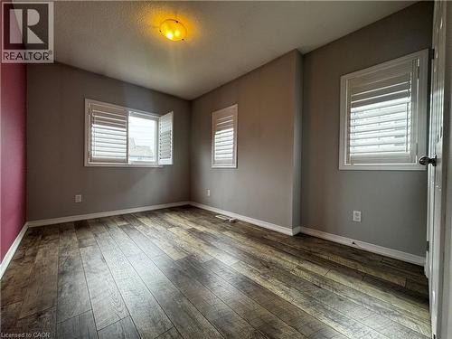 Spacious room featuring wood-finish flooring, multiple windows with white plantation shutters, a contrasting accent wall, and a flush-mount ceiling light fixture - 13 Sorrento Street, Kitchener, ON - Indoor Photo Showing Other Room