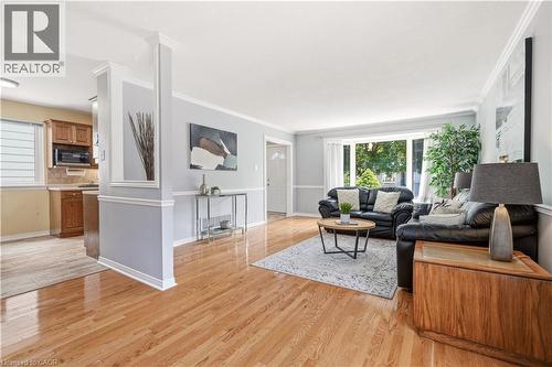 Living area with wood-finish flooring, a broad picture window, light gray walls with chair rail molding, and white crown molding - 4277 Longmoor Drive, Burlington, ON 