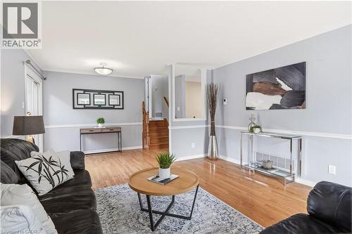 Spacious living area featuring wood-finish flooring, light gray wall tones with white trim, and a built-in staircase with wood risers and handrails - 4277 Longmoor Drive, Burlington, ON 