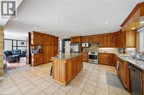 Spacious kitchen featuring a central island with a granite countertop, extensive wood cabinetry, tile flooring, stainless steel appliances, and recessed lighting - 39 Elodia Court, Hamilton, ON 