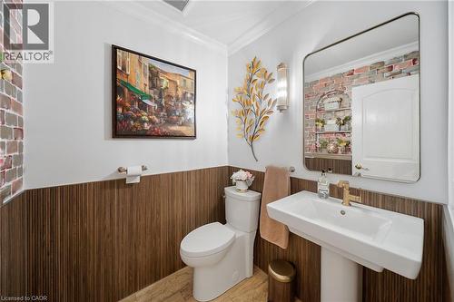 Pedestal sink with gold-tone faucet, wood-finish wainscoting, and a rectangular mirror - 39 Elodia Court, Hamilton, ON 