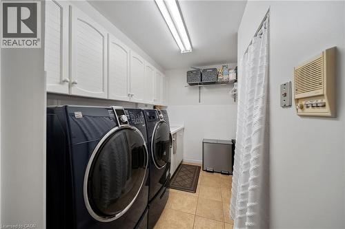 Laundry area featuring white shaker-style cabinetry, a white countertop, wall-mounted shelving, and tan tile flooring - 39 Elodia Court, Hamilton, ON 