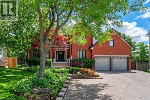 Red brick exterior featuring a multi-car driveway, two-car garage, mature front yard landscaping, stone retaining wall, and a raised entry with a dark-paneled front door - 39 Elodia Court, Hamilton, ON 