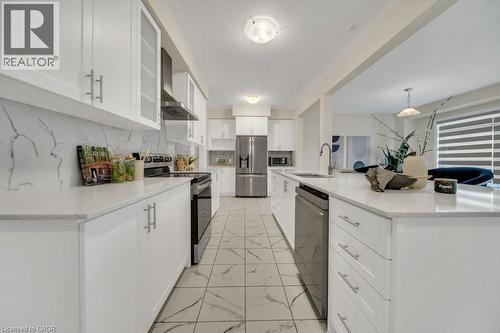 Kitchen featuring appliances with stainless steel finishes, tasteful backsplash, white cabinets, wall chimney range hood, and light marble finish flooring - 285 Broadacre Drive, Kitchener, ON 