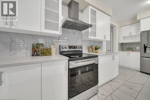 Kitchen featuring appliances with stainless steel finishes, wall chimney range hood, light marble finish flooring, tasteful backsplash, and white cabinetry - 285 Broadacre Drive, Kitchener, ON 