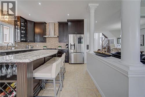 Kitchen featuring dark wood cabinetry, stainless steel appliances, a tile backsplash, and a large central island with a light-colored countertop - 37 Davinci Boulevard, Hamilton, ON 